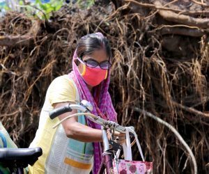 epa08436888 A commuter wears a protective face mask as she passes an uprooted tree after Cyclone Amphan hit Bengal; in Kolkata, India, 22 May 2020.  A massive water crisis faces the city due to disrupted electricity supply lines. According to media reports, 80 people died in Bengal after cyclone Amphan hit the Bengal.  EPA/PIYAL ADHIKARY