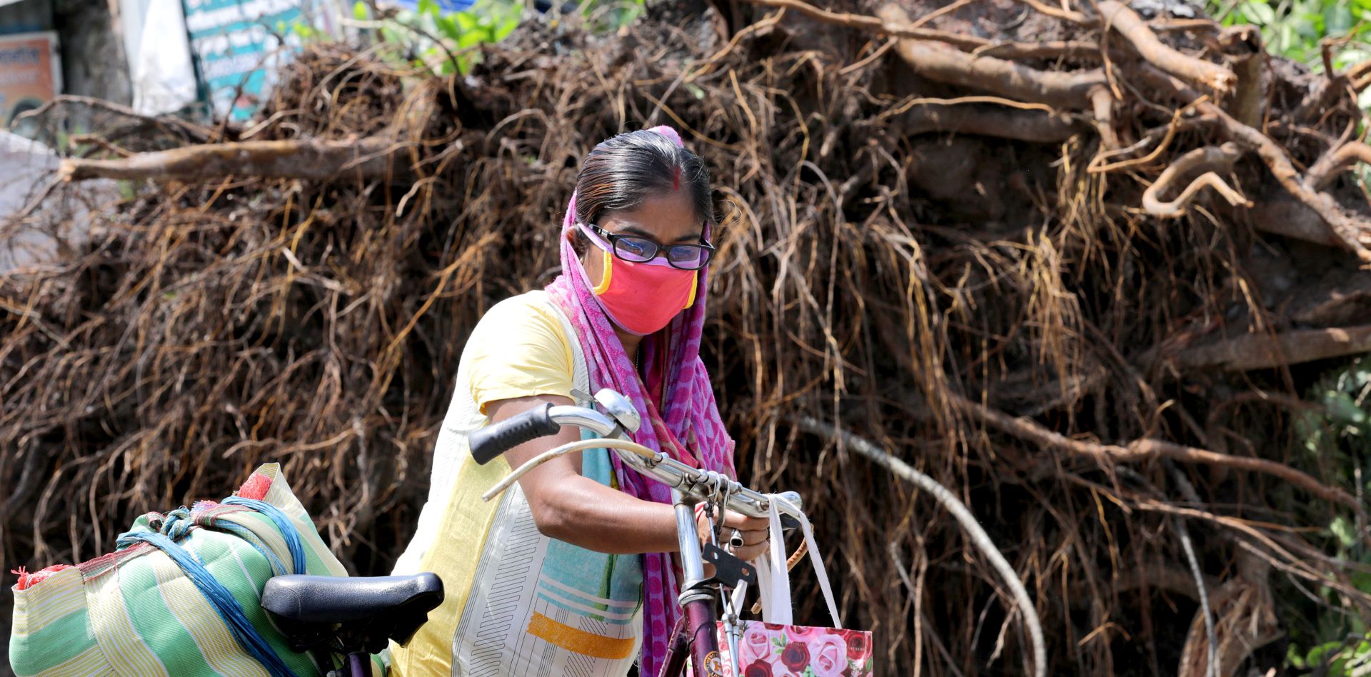 epa08436888 A commuter wears a protective face mask as she passes an uprooted tree after Cyclone Amphan hit Bengal; in Kolkata, India, 22 May 2020.  A massive water crisis faces the city due to disrupted electricity supply lines. According to media reports, 80 people died in Bengal after cyclone Amphan hit the Bengal.  EPA/PIYAL ADHIKARY