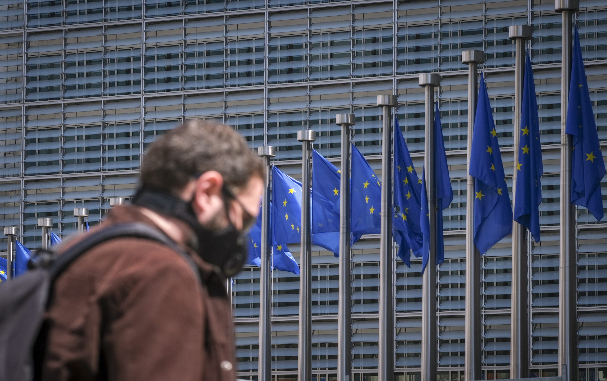 epa08443018 A man wearing a face mask walks in front of the European Commission flags at the Berlaymont building headquarters in Brussels, Belgium, 25 May 2020. Countries around the world are gradually easing COVID-19 lockdown restrictions in an effort to restart the economy and help people in their daily routines.  EPA/OLIVIER HOSLET