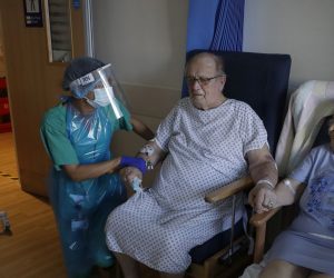 epa08436356 Coronavirus patients George Gilbert, 85 and his wife Domneva Gilbert 84, hold hands during a short visit, they are being treated in different areas, both are part of the TACTIC-R trial, at Addenbrooke's hospital in Cambridge, Britain, 21 May 2020. The new trial known as TACTIC-R is testing whether existing drugs will help prevent the body's immune system from overreacting, which scientists hope could prevent organ failure and death in COVID-19 patients.  EPA/Kirsty Wigglesworth / POOL