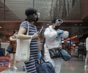 epa08474228 Travellers wearing protective masks and overalls walk through the departure hall of Changi Airport in Singapore, 09 June 2020. Singapore's Changi Airport will resume transit flights for travellers and will launch a 'green lane' to various cities in China such as Shanghai, Tianjin, Chongqing, Guangdong, Jiangsu and Zhejiang, in order to facilitate essential business and official travel between the two countries.  EPA/WALLACE WOON