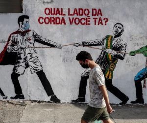 epa08504708 A man passes in front of a graffiti that represents Brazilian President Jair Bolsonaro and a figure that represents the novel coronavirus COVID-19 pulling a rope against health workers with a message that says: 'Which side of the rope are you on?' in Sao Paulo, Brazil, 23 June 2020.  EPA/Sebastiao Moreira