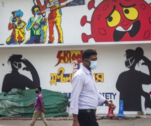 epa08513536 Bangladeshi people wearing face masks walk in front of graffiti in Dhaka, Bangladesh, 28 June 2020. Countries around the world are taking increased measures to stem the spread of the SARS-CoV-2 coronavirus which causes the COVID-19 disease.  EPA/MONIRUL ALAM