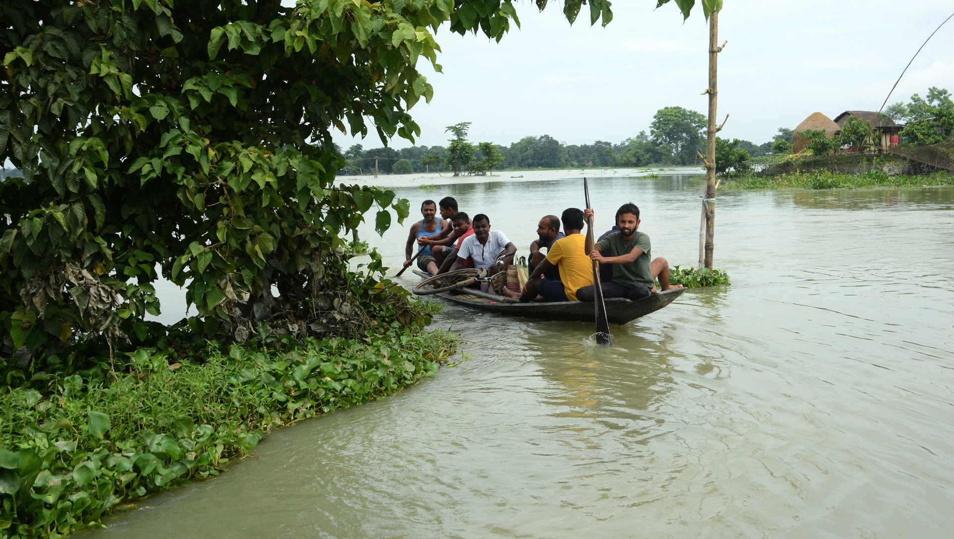 epa08551703 Villagers use a boat to cross a flooded area in Morigaon district of Assam, India, 17 July 2020. According to news reports, Assam state continues to battle with flood situation which has left over three million people affected by it and at least sixty dead.  EPA/STR