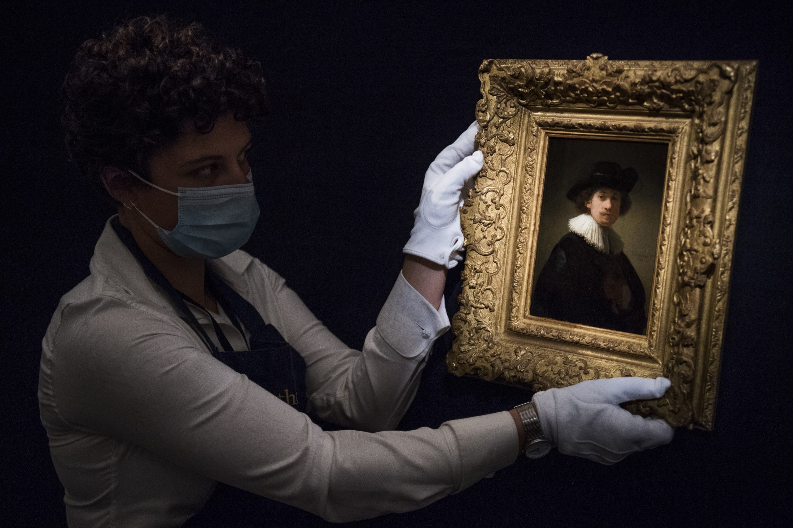 epa08563615 A worker poses with 'Self-portrait, wearing a ruff and black hat' by Dutch artist Rembrandt Van Rijn at the 'Rembrandt to Richter' art sale at Sotheby's auction house in London, Britain, 23 July 2020 (issued 24 July 2020). Works from Old Masters, Impressionist & Modern Art, Modern & Post-War British Art are on display at Sotheby's London ahead of a one-off auction on July 28.  EPA/NEIL HALL