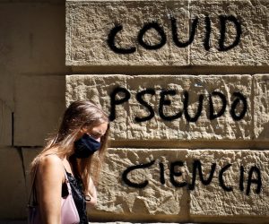 epa08612717 A woman walks past a graffiti reading 'Coronavirus Pseudo-Science' in a street in San Sebastian Basque Country, northern Spain, 19 August 2020. A movement doubting the existence of coronavirus pandemic is appearing in Spain, with several demonstrations, held last weekend in several cities, to protest against the compulsory use of face mask and measures imposed by Government to deal with COVID-19 virus disease.  EPA/Javier Etxezarreta