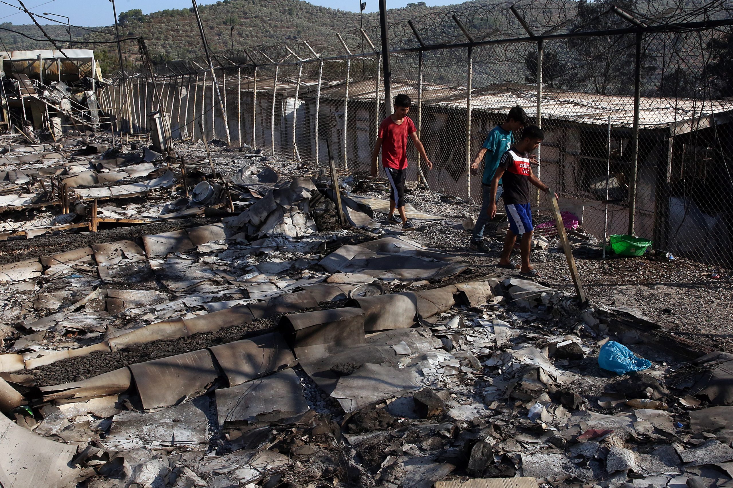 epa08656942 Asylum seekers walk among debris in the Moria refugees camp on the island of Lesbos, Greece, 09 September 2020. According to reports, a fire broke out at Moria Camp early on 09 September, after approximately 35 refugees, who had tested positive for COVID-19, refused to move into isolation with their families.  EPA/ORESTIS PANAGIOTOU