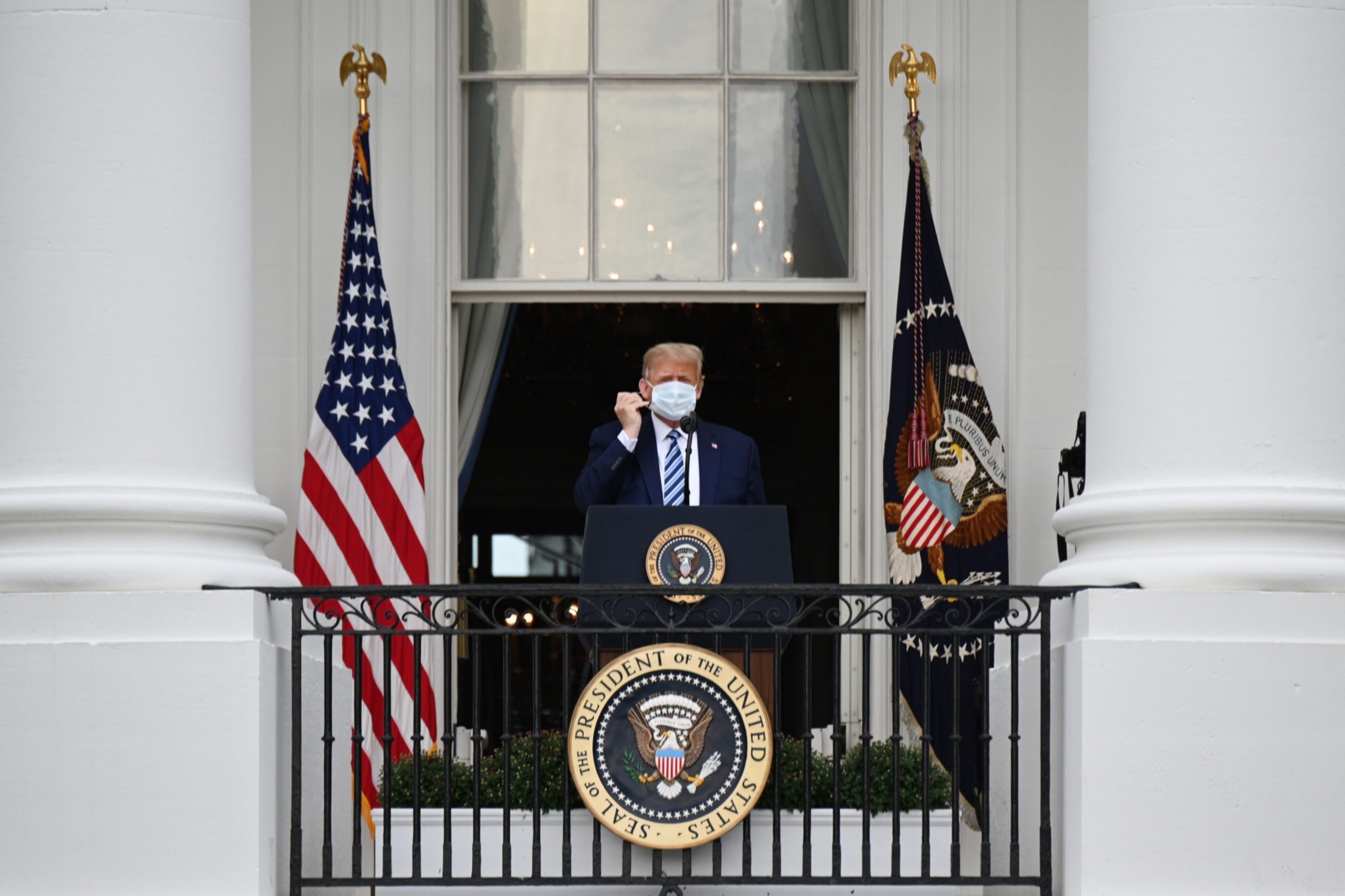 epa08734758 US President Donald J. Trump removes a protective mask ahead of speaking from the Truman Balcony of the White House in Washington, DC, USA, on 10 October 2020. Trump, making his first public appearance since returning from a three-day hospitalization for Covid-19, is setting the stage for a return to the campaign trail even as questions remain about whether he's still contagious.  EPA/Erin Scott / POOL