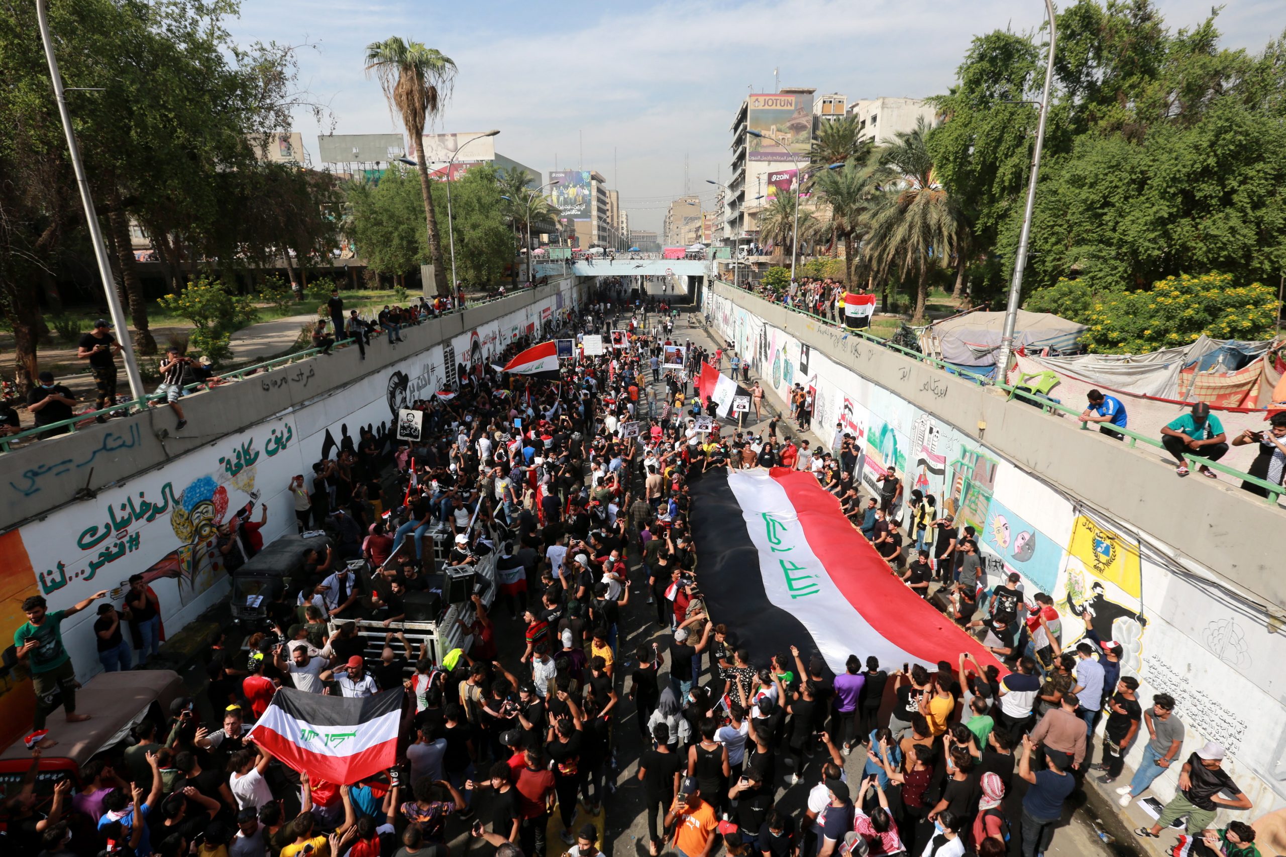 epa08773516 Iraqi protesters carry national flags as they protest in Baghdad, Iraq, 25 October 2020. Dozens of protesters were wounded in clashes with security forces after a demonstration which was held to mark the 25 October 2019 mass protests that resumed a day after some 50 protesters were killed and injured when attempting to enter Baghdad's heavily fortified 'Green Zone', and demand to put those on trial who are responsible for the killed protesters.  EPA/AHMED JALIL