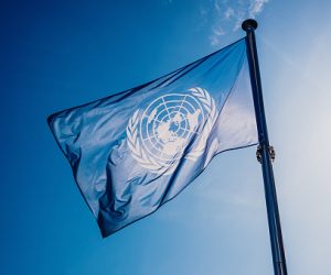 UN flag waved against the sun and blue sky.