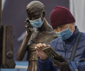 epa08929712 A man uses his phone next to a statue with a mask in Shanghai, China, 10 January 2021. Two Chinese cities near Beijing, Shijiazhuang and Xingtai, are locked down after a spike in Covid-19 cases. Over 300 new cases of the coronavirus disease were confirmed in Hebei province this week, according to the National Health Commission of China.  EPA/ALEX PLAVEVSKI