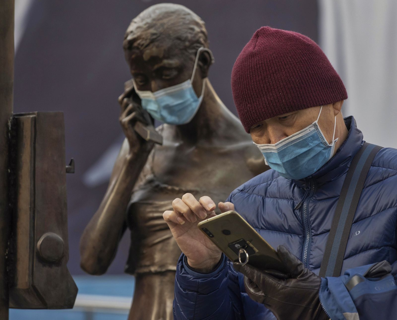 epa08929712 A man uses his phone next to a statue with a mask in Shanghai, China, 10 January 2021. Two Chinese cities near Beijing, Shijiazhuang and Xingtai, are locked down after a spike in Covid-19 cases. Over 300 new cases of the coronavirus disease were confirmed in Hebei province this week, according to the National Health Commission of China.  EPA/ALEX PLAVEVSKI