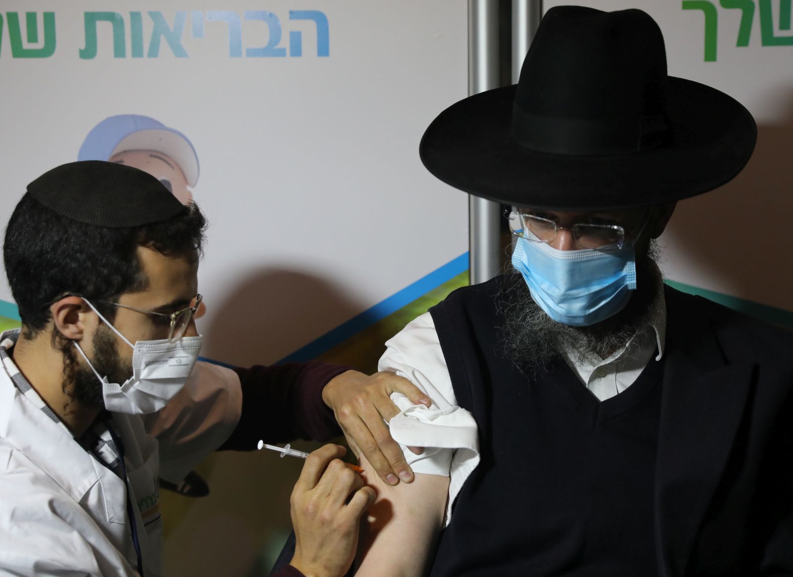epa08937701 An ultra-orthodox Jewish man receives a coronavirus COVID-19 pandemic vaccine by a male nurse in Jerusalem, Israel, 14 January 2021. Media report that Israel is on a massive nationwide COVID-19 vaccination campaign, with more than two million people already got the first dose.  EPA/ABIR SULTAN