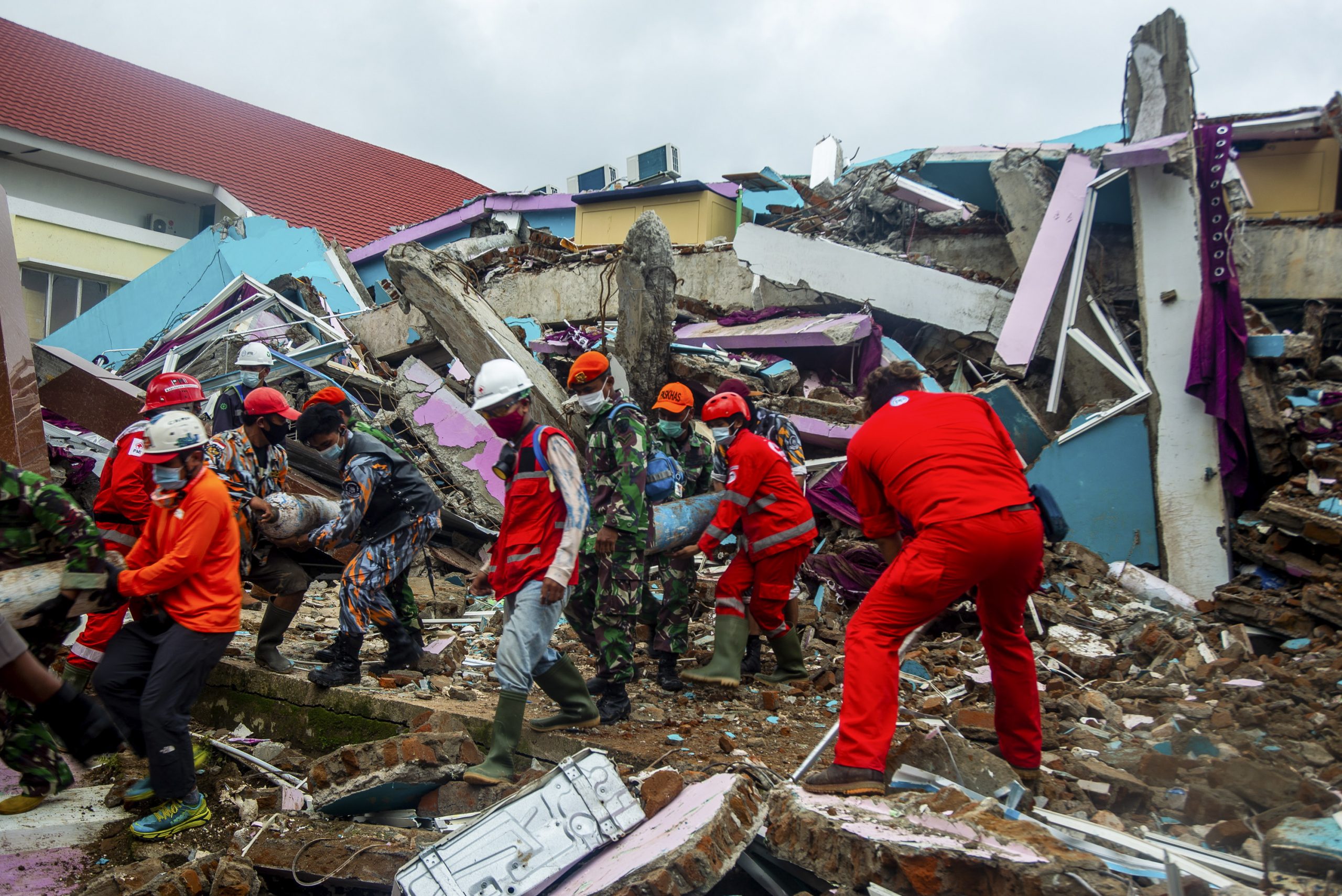 epa08943004 Rescuers and volunteers carry tubes out of the ruin of a collapsed building hit by the 6.2 magnitude earthquake in Mamuju, West Sulawesi, Indonesia, 17 January 2021. At least 56 people died and hundreds were injured after a 6.2 earthquake struck Sulawesi island on 15 January.  EPA/IQBAL LUBIS