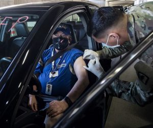 epa09030222 US National Guard medic Lake Granado vaccinates a patient against Covid-19 in his car at the Convention Center drive-thru vaccination Site amid coronavirus pandemic in Long Beach, South of Los Angeles, California, USA, 22 February 2021.  EPA/ETIENNE LAURENT