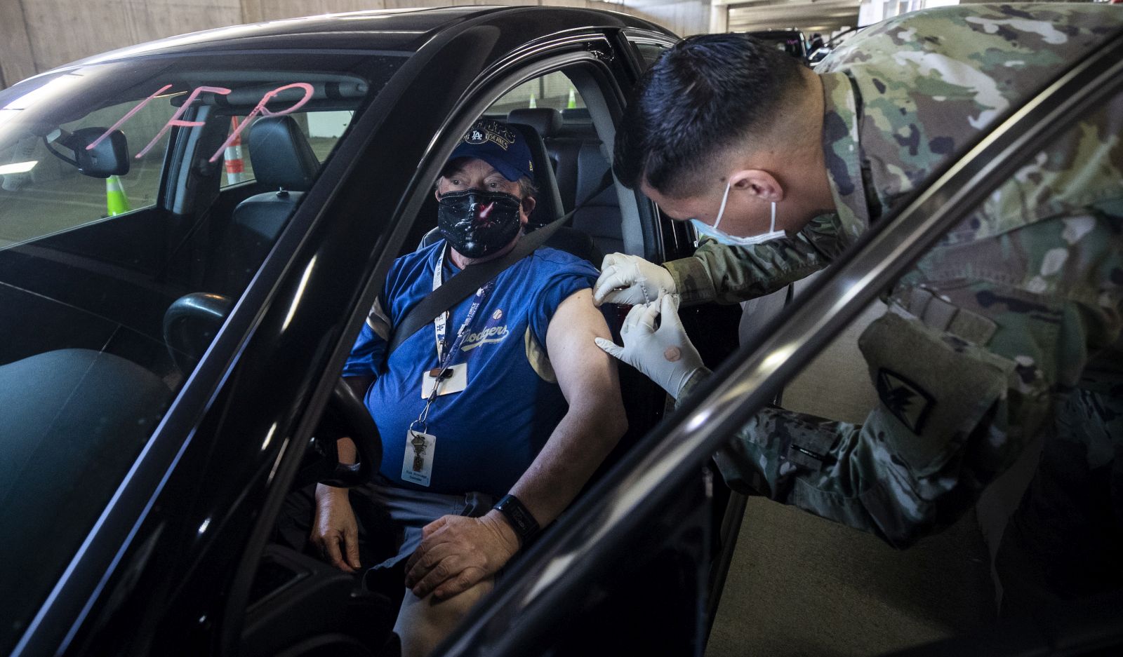 epa09030222 US National Guard medic Lake Granado vaccinates a patient against Covid-19 in his car at the Convention Center drive-thru vaccination Site amid coronavirus pandemic in Long Beach, South of Los Angeles, California, USA, 22 February 2021.  EPA/ETIENNE LAURENT
