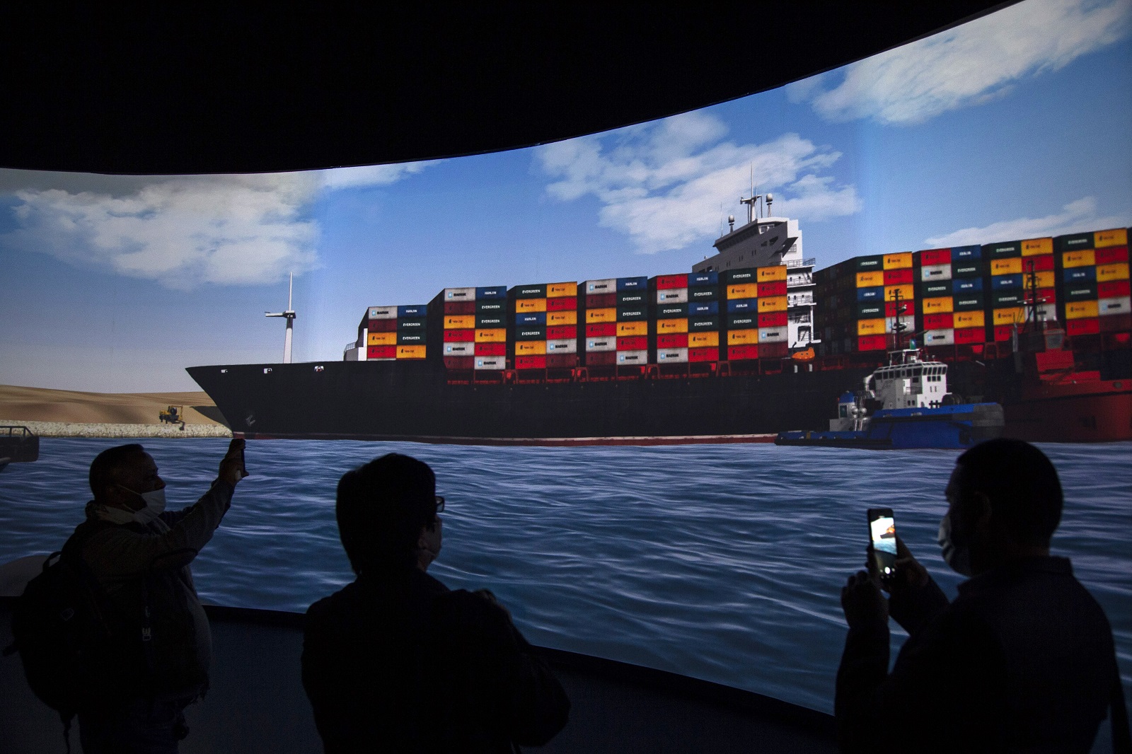 epa09104782 Reporters stand in front of a screen displaying a simulation of the pulling of Ever Given container ship in the Suez Canal, demonstrated during a press conference at the Maritime Training and Simulation Centre of the Suez Canal Authority in Ismailia, Egypt, 29 March 2021. The Suez Canal Authority announced on 29 March that the large container ship, which ran aground in the Suez Canal on 23 March, was partly refloated after responding to the pulling maneuvers and the back of the ship is now 102 meters away from the bank of the canal.  EPA/Mohamed Hossam