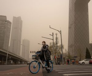 epa09102495 A woman wearing a protective face mask waits on a bicycle in the Central Business District (CBD) area amid a sandstorm in Beijing, China, 28 March 2021. A new sandstorm hit Beijing on 28 March as the city was already in the grip of high air pollution levels.  EPA/ROMAN PILIPEY