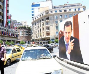 epa09226908 Syrians pass near presidential election poster of incumbent President Bashar Assad on the eve of elections in Damascus, Syria, 25 May 2021. Election campaigning for the candidates come to an end on 25 May as the electoral silence starts ahead of the elections, scheduled for 26 May 2021, in which three candidates, including President Assad, are running up for the post.  EPA/YOUSSEF BADAWI
