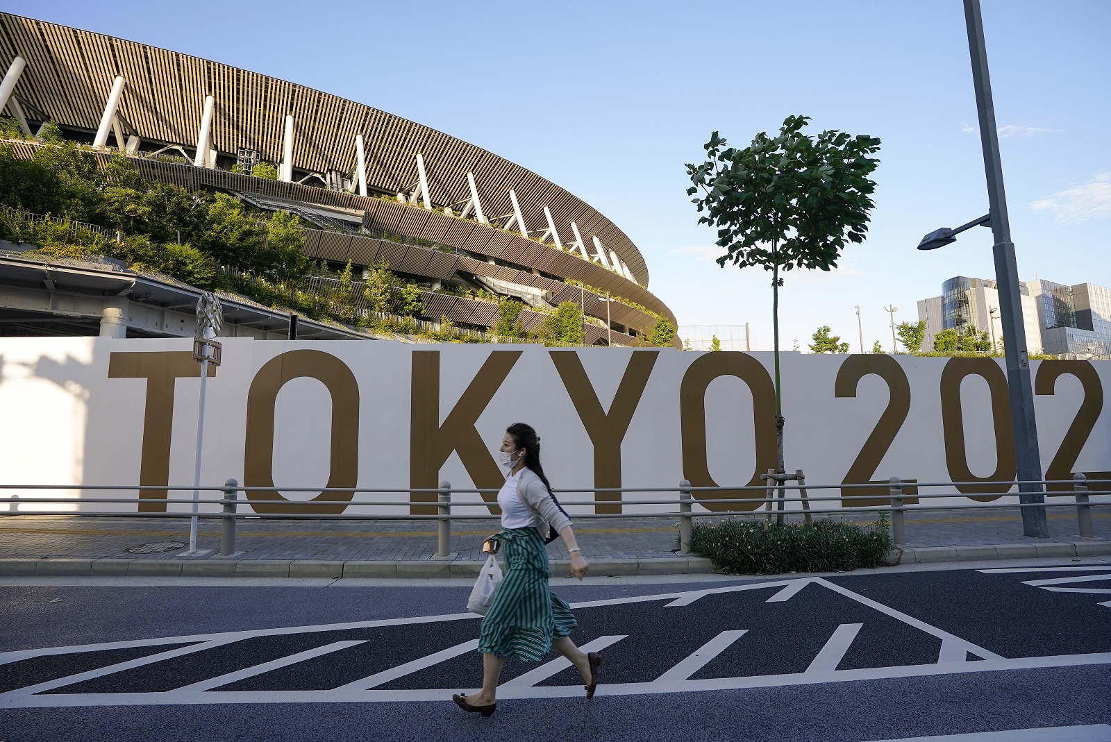 epa09279196 A pedestrian walks past the New National Stadium, or the Olympic Stadium for the Opening Ceremony, Closing Ceremony and Athletics event, in Tokyo, Japan, 17 June 2021, after the Japanese government decided to lift the COVID-19 state of emergency as scheduled to end on 20 June 2021, in nine prefectures including Tokyo. The government also decided to keep restrictions to avoid a rebound of infections before the Tokyo Olympic Games.  EPA/KIMIMASA MAYAMA