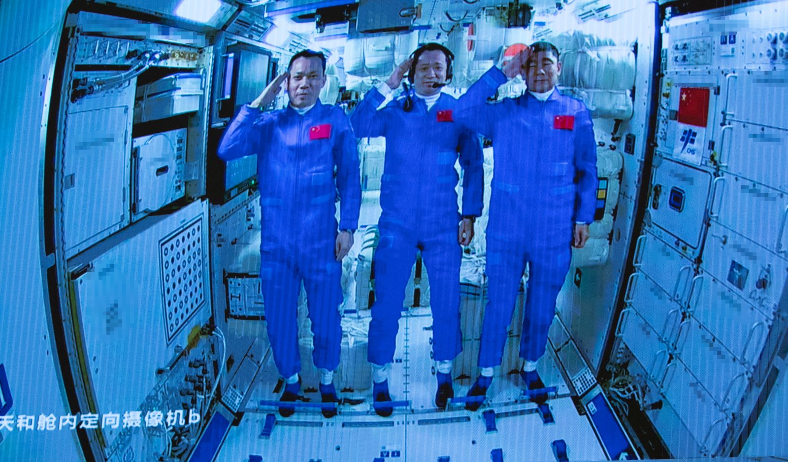 epa09281811 A screen image made available by Xinhua News Agency captured at the Beijing Aerospace Control Center shows three Chinese astronauts onboard the Shenzhou-12 spaceship saluting after entering the Tianhe space station core module in Beijing, China, 17 June 2021 (issued 18 June 2021). China launched the Shenzhou-12 spacecraft carrying three crew members Tang Hongbo, Nie Haisheng, and Liu Boming to the orbiting Tianhe core module for a three-month mission on 17 June. The mission is China's first manned spaceflight in almost five years.  EPA/XINHUA/JIN LIWANG MANDATORY CREDIT EDITORIAL USE ONLY/NO SALES