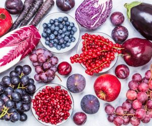 Purple and red color fruits and vegetables ingredients top view on rustic white background.