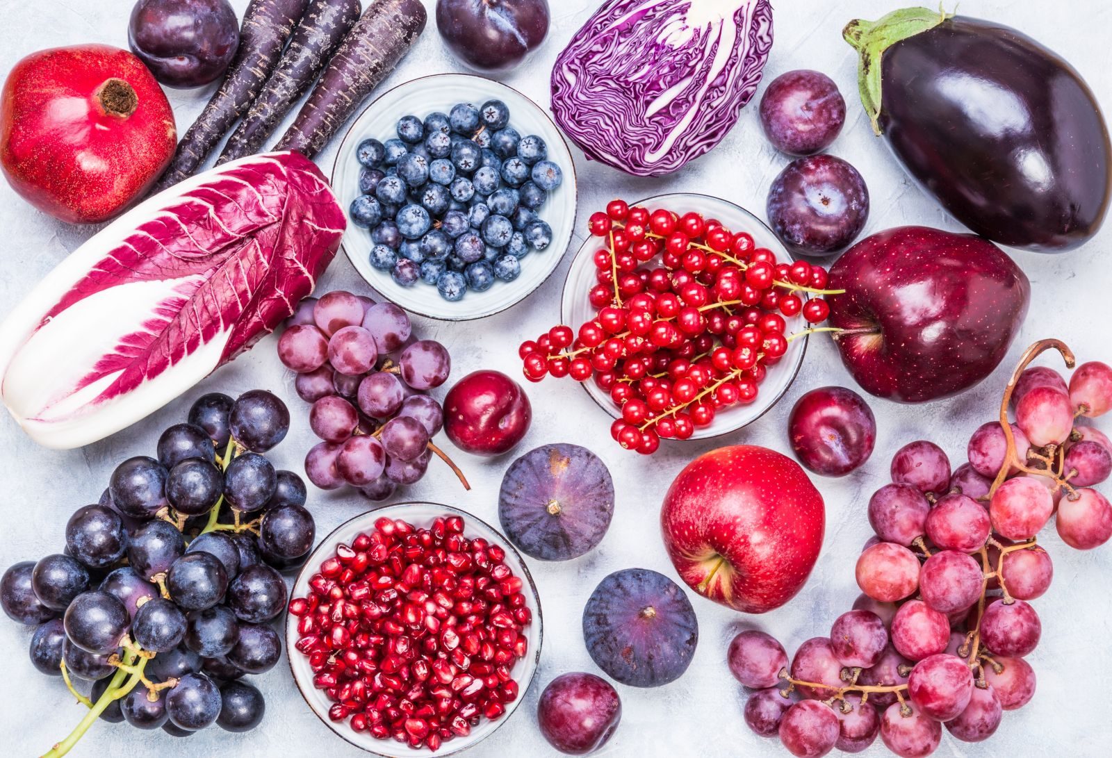 Purple and red color fruits and vegetables ingredients top view on rustic white background.
