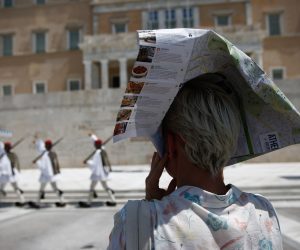 epa09385487 A woman covers head with a tourist flyer of Athens to protect herself from the sun as Greek Presidential Guard perform during a heatwave in central Athens, Greece, 01 August 2021. Temperatures are expected to reach up to 44 degrees Celsius in mainland Greece in the coming days, the National Meteorological Service (EMY) has warned the public in an emergency bulletin.  EPA/YANNIS KOLESIDIS