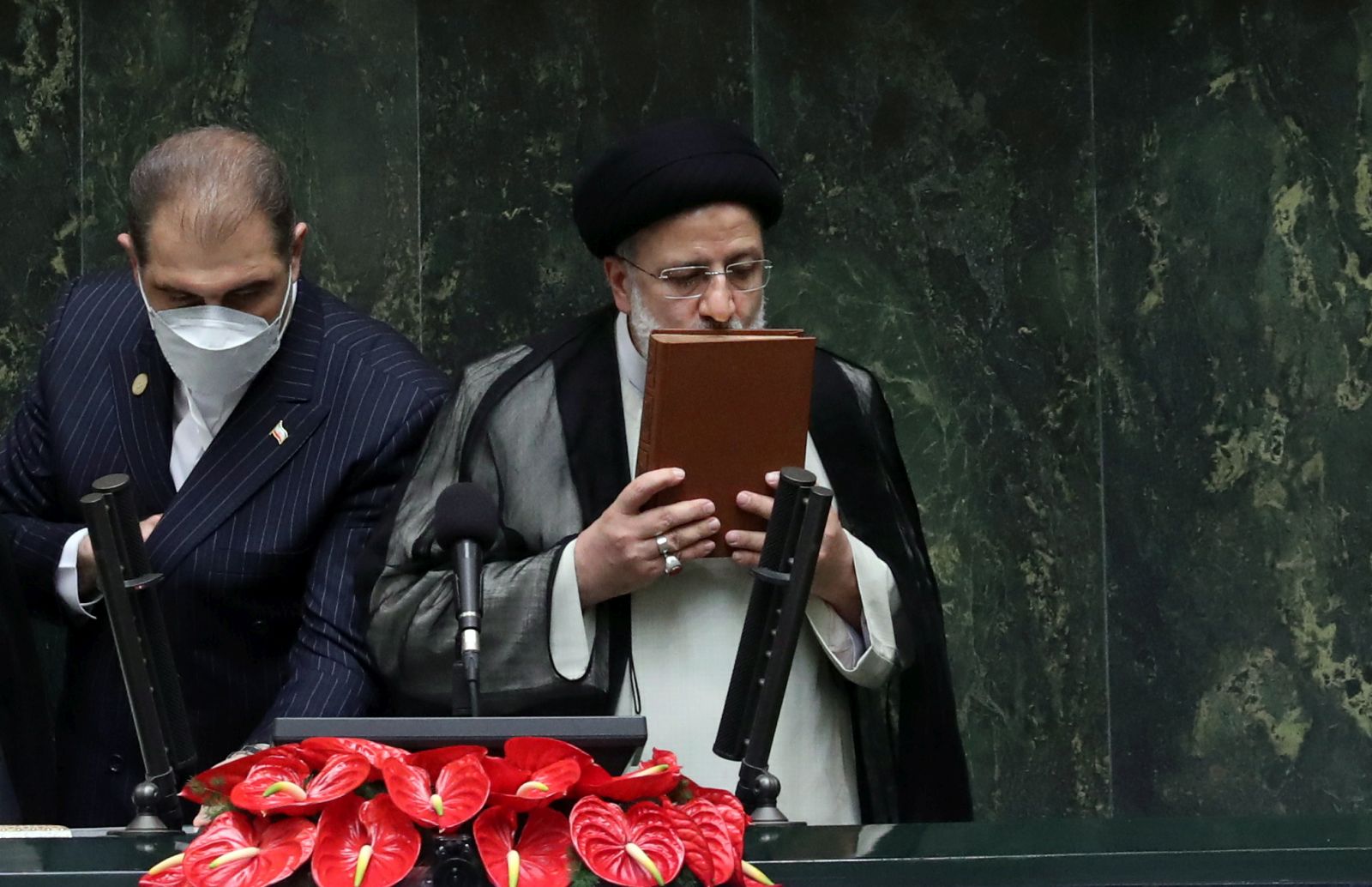 epa09398424 Iranian President Ebrahim Raisi (R) kisses the holy Koran after being sworn-in for his first four-year term of presidency at the parliament in Tehran, Iran, 05 August 2021.  Iran's new president Ebrahim Raisi was sworn in on 05 August before parliament in Tehran in a ceremony that foreigners attended for the second time since the Islamic Revolution in 1979. Raise is to present his cabinet to the 290-seat parliament for approval in the next week.  EPA/ABEDIN TAHERKENAREH