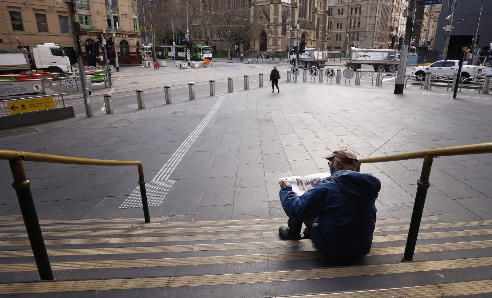 epa09408982 A man reads the newspaper on the steps of Flinders Street Station in Melbourne, Victoria, Australia, 11 August 2021. Regional Victoria's lockdown is over but people in Melbourne are still days from finding out when theirs will end.  EPA/DANIEL POCKETT AUSTRALIA AND NEW ZEALAND OUT