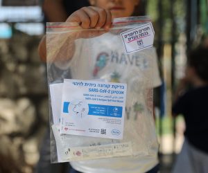 epa09438081 An Israeli girl holds SARS CoV-2 Antigen self Test delivered by the teachers outside a school in Jerusalem, 31 August 2021. Israel started a national quick covid-19 test campaign to kids from 3 to 12 years old in order to safely reopen the schools on September 01  EPA/ABIR SULTAN