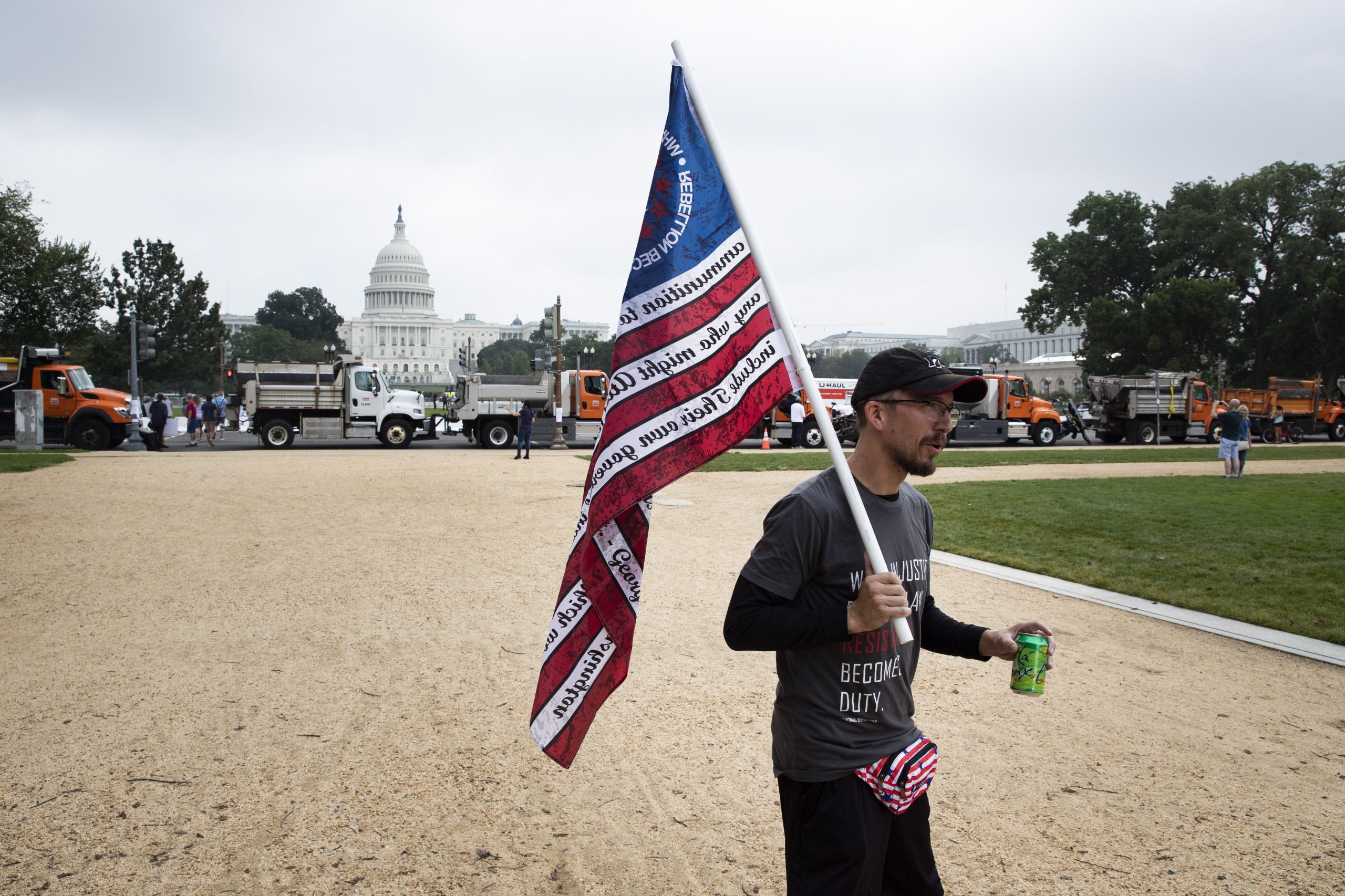 epa09475095 A supporter of the 'Justice for J6' protest carries a flag near the National Mall in front of trucks being used as a barricade by authorities as people begin to arrive for the 'Justice for J6' protest, on Capitol Hill in Washington, DC, USA, 18 September 2021. A protest called 'Justice for J6' has been planned to show support for people jailed for their role in the 06 January 2021 attack on the Capitol.  EPA/MICHAEL REYNOLDS