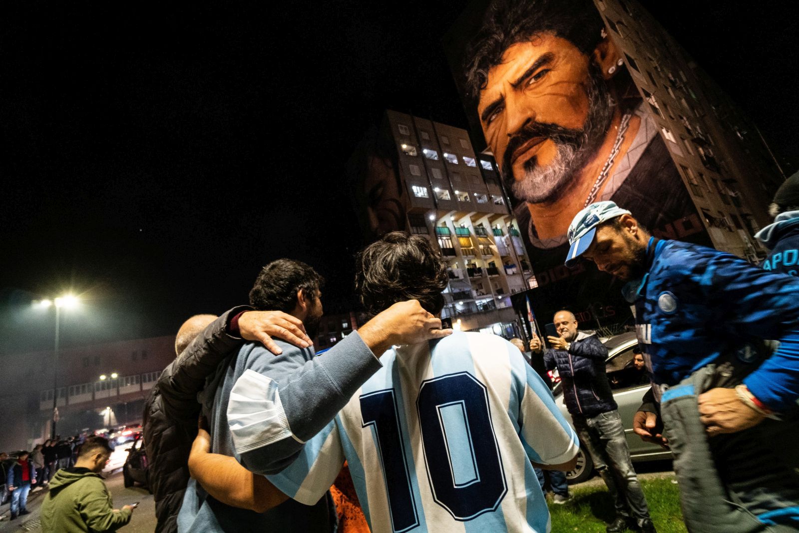 epa09555570 Fans celebrate Diego Armando Maradona's birthday anniversary next to a mural, made by Italian-Dutch street artist Jorit, depicting the late Argentine football legend in Naples, southern Italy, late 30 October 2021. Maradona passed away on 25 November 2020 at the age of 60.  EPA/CESARE ABBATE