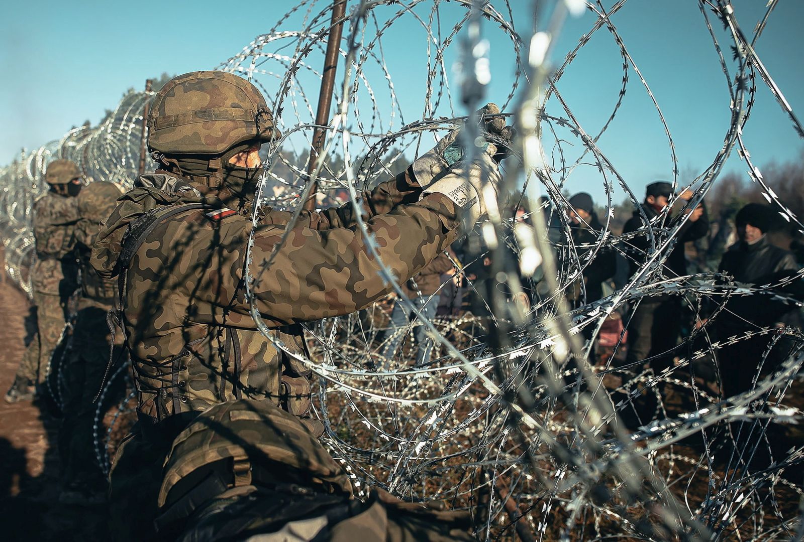 epa09578267 A handout photo made available by Polish Territorial Defence Force shows Polish soldiers guard the fence during 'Operation Strong Support' near the Polish-Belarusian border crossing in Kuznica, eastern Poland, 09 November 2021 (issued 12 November 2021). According to Polish Border Guard, over a thousand refugees, who want to obtain asylum in the European Union have been trapped at low temperatures at the border Polish-Belarusian border.  EPA/IREK DOROZANSKI / POLISH TERRITORIAL DEFENCE FORCE / HANDOUT POLAND OUT HANDOUT EDITORIAL USE ONLY/NO SALES