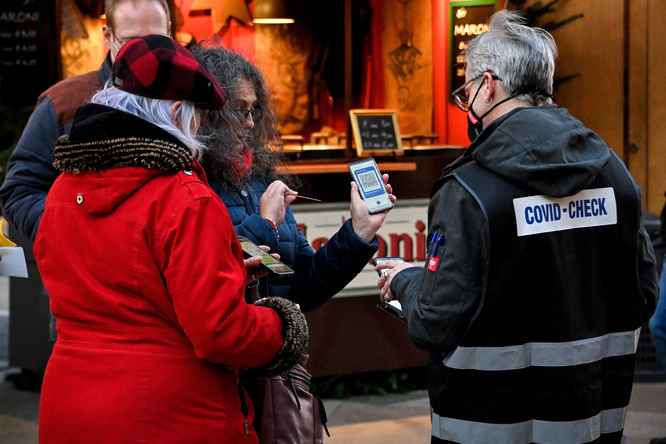 epa09597967 A 'Covid-Check' inspector (R) checks digital vaccination certificates on smartphones of Christmas market visitors nearby the Cathedral in Cologne, Germany, 22 November 2021. Germany is dealing with a high number of new coronavirus COVID-19 infections.  EPA/SASCHA STEINBACH