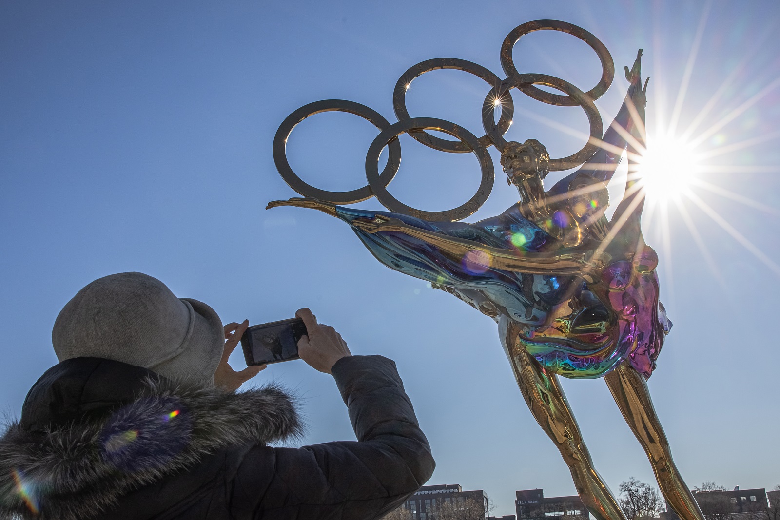 epa09614024 A woman takes photos with her mobile phone of a figure skating sculpture erected for the Beijing 2022 Winter Olympics, at the Shougang Industrial Park, which will be used as a venue for hosting sport and other events during Beijing 2022 Winter Olympics, in Beijing, China, 01 December 2021. According to China's epidemiologist experts, the new Omicron COVID-19 variant, which poses a high risk globally, at this moment wouldn't have a strong impact on China, which is scheduled in two months to host The 2022 Beijing Winter Olympics followed by the Paralympics.  EPA/ROMAN PILIPEY