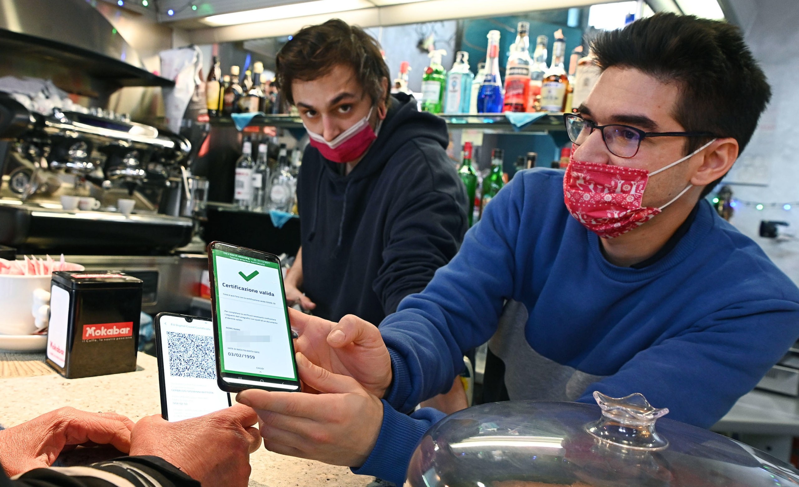 epaselect epa09657886 A bar owner checks the Green Pass of customer at the bar counter in Turin, Italy, 27 December 2021. The Italian government on 24 December imposed a series of new COVID-19 prevention measures, including the obligation to wear facemasks outdoors, and reduced the duration of the 'Super Green Pass' health certificate, which is obligatory for all customers who eat food or have a drink inside a bar or restaurant.  EPA/ALESSANDRO DI MARCO