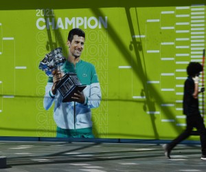 epa09679554 A person walks past an image of Serbian tennis player Novak Djokovic on a wall at Melbourne Park in Melbourne, Australia, 12 January 2022. Djokovic, who is the number one tennis player in the world, waits to learn if his visa will be cancelled.  EPA/JAMES ROSS  AUSTRALIA AND NEW ZEALAND OUT