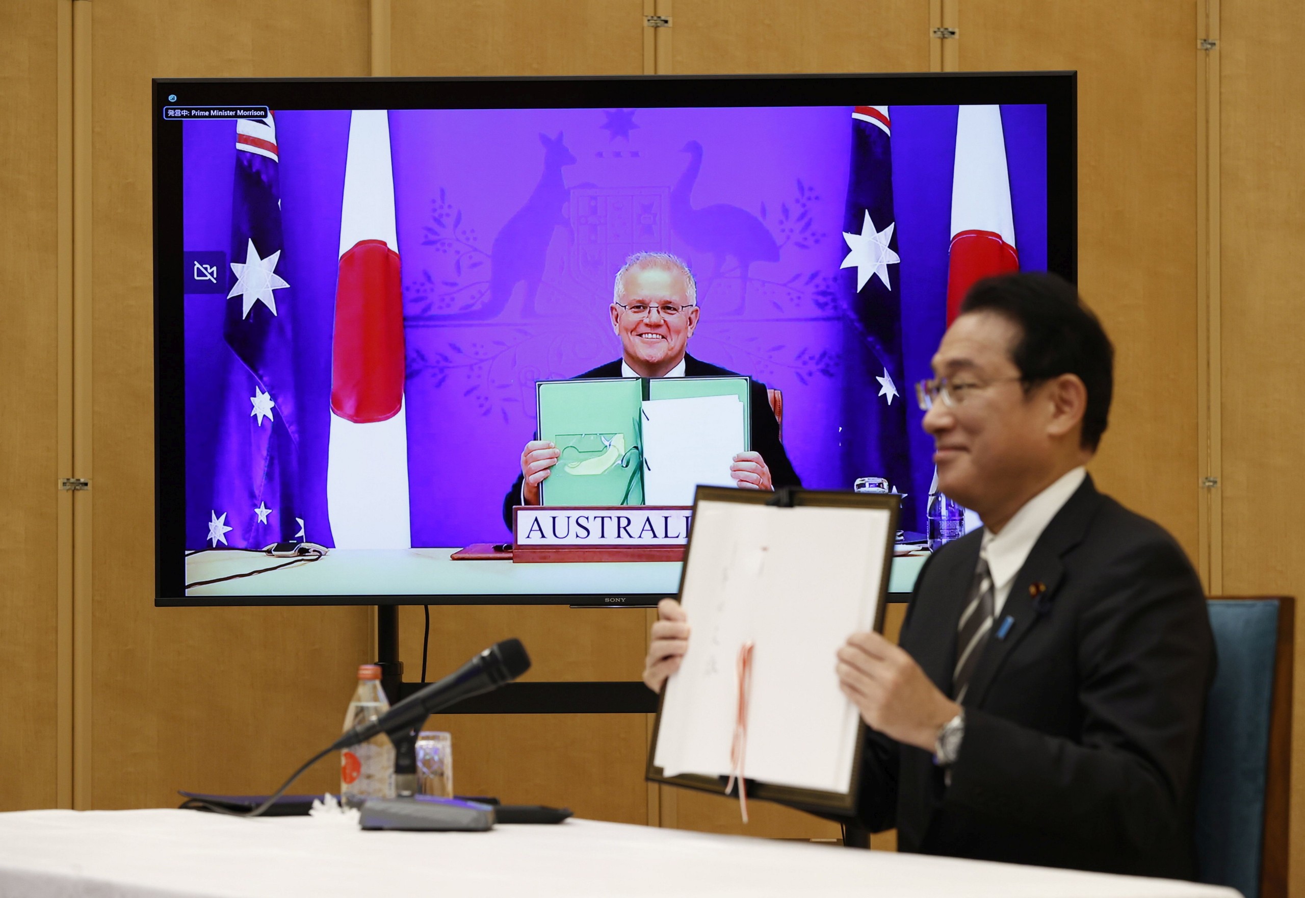 epa09668940 Japan's Prime Minister Fumio Kishida (R) and Australia's Prime Minister Scott Morrison (on video) show off signed documents during their video signing ceremony of the bilateral reciprocal access agreement at Kishida's official residence in Tokyo, Japan, 06 January 2022.  EPA/ISSEI KATO / POOL