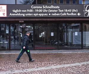 epa09719614 A man walks past a billboard displaying the opening hours of a local Corona test center in Garmisch-Partenkirchen, Germany, 31 January 2022.  EPA/PHILIPP GUELLAND