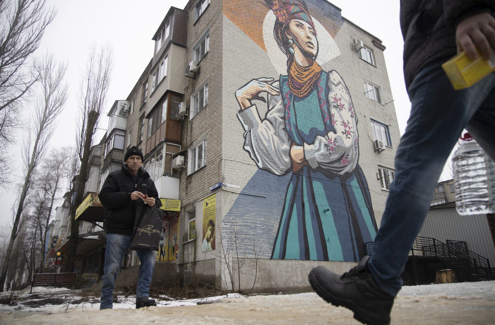 epa09725712 Locals walk in a street in front of a big mural on a building wall in the small Ukrainian city of Avdiivka not far from the pro-Russian militants-controlled city of Donetsk, Ukraine, 03 February 2022. Locals adapted to live a normal life not far from a front line amid escalation on the Ukraine - Russian border.  EPA/STANISLAV KOZLIUK