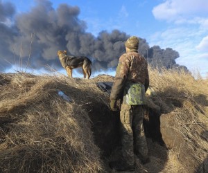 epa09788439 A Ukrainian serviceman and his dog stands in a position looking at smoke from a burned petroleum storage depot behind after a Russian missile attacked near Kiev, Ukraine, 27 February 2022. Russian troops entered Ukraine on 24 February prompting the country's president to declare martial law and triggering a series of announcements by Western countries to impose severe economic sanctions on Russia.  EPA/ALISA YAKUBOVYCH
