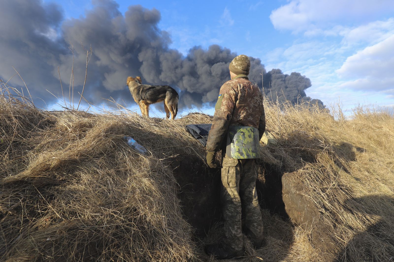epa09788439 A Ukrainian serviceman and his dog stands in a position looking at smoke from a burned petroleum storage depot behind after a Russian missile attacked near Kiev, Ukraine, 27 February 2022. Russian troops entered Ukraine on 24 February prompting the country's president to declare martial law and triggering a series of announcements by Western countries to impose severe economic sanctions on Russia.  EPA/ALISA YAKUBOVYCH