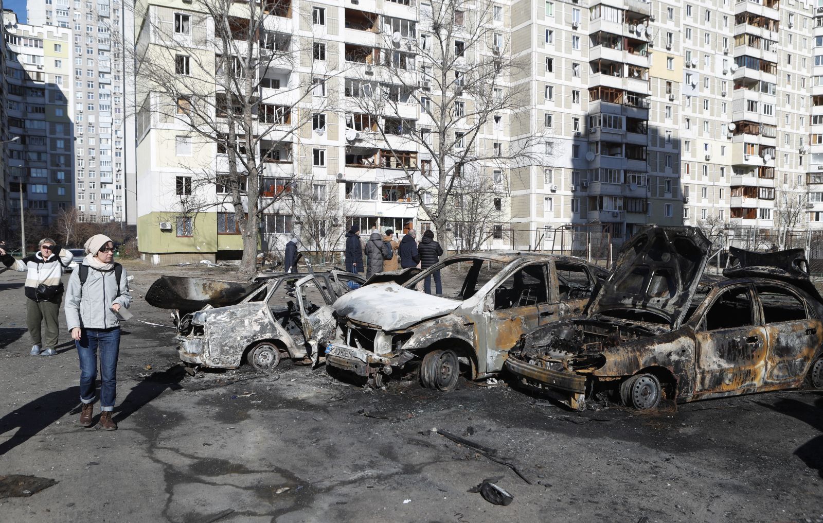 epa09791843 People walk past burned cars a day after a shelling on a residential area in Kiev, Ukraine, 28 February 2022. Russian troops entered Ukraine on 24 February prompting the country's president to declare martial law and triggering a series of severe economic sanctions imposed by Western countries on Russia.  EPA/SERGEY DOLZHENKO