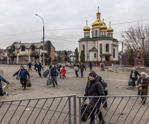 epa09807427 Residents run to cross a road with their luggage next to a damaged church as people flee from the frontline town of Irpin, Kyiv (Kiev) region, Ukraine, 07 March 2022. Irpin, the town which is located near Kyiv city had heavy fightings for almost a week between Ukrainian and Russian militaries forcing thousands of people to escape from the town.  EPA/ROMAN PILIPEY