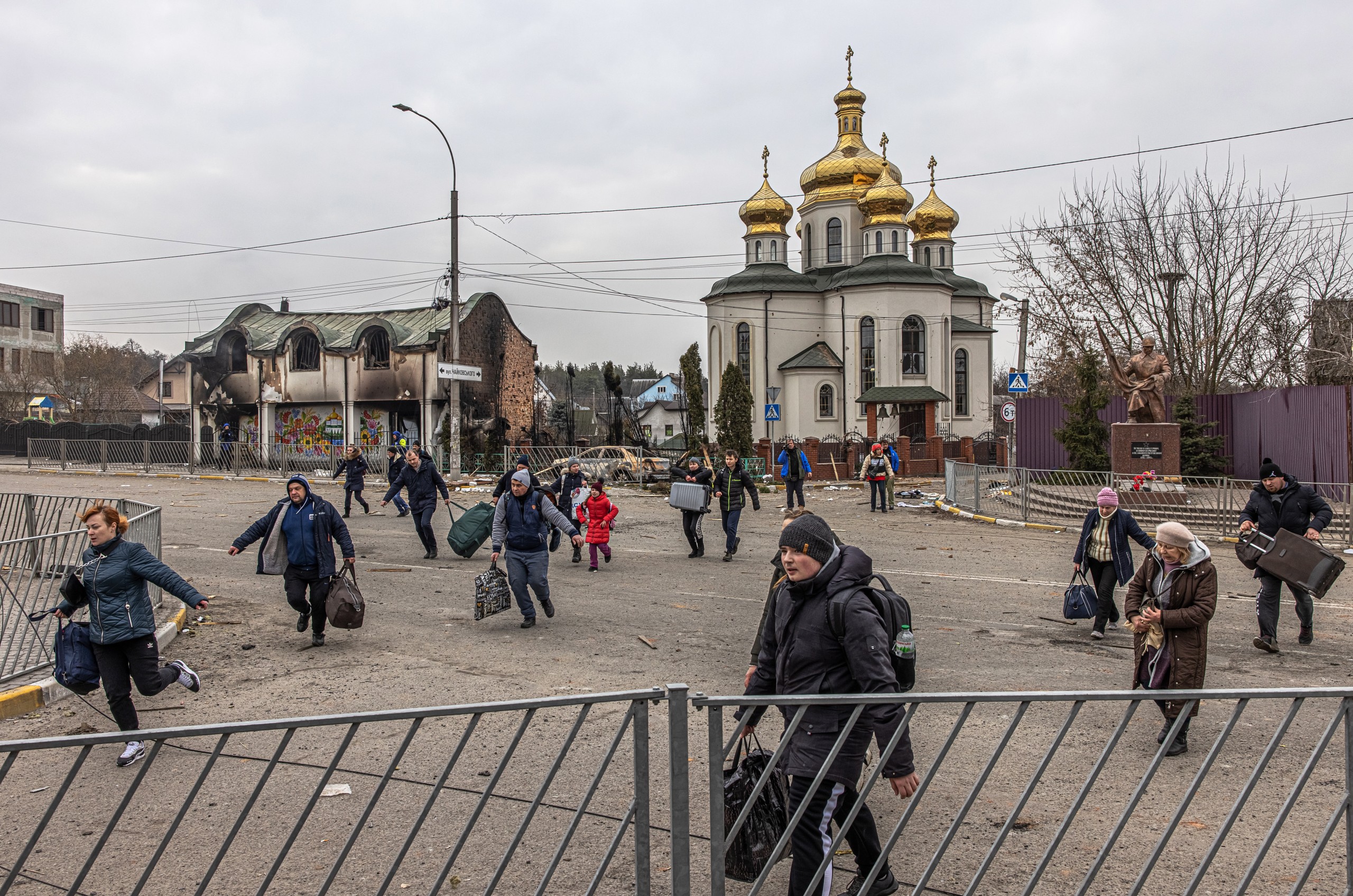 epa09807427 Residents run to cross a road with their luggage next to a damaged church as people flee from the frontline town of Irpin, Kyiv (Kiev) region, Ukraine, 07 March 2022. Irpin, the town which is located near Kyiv city had heavy fightings for almost a week between Ukrainian and Russian militaries forcing thousands of people to escape from the town.  EPA/ROMAN PILIPEY