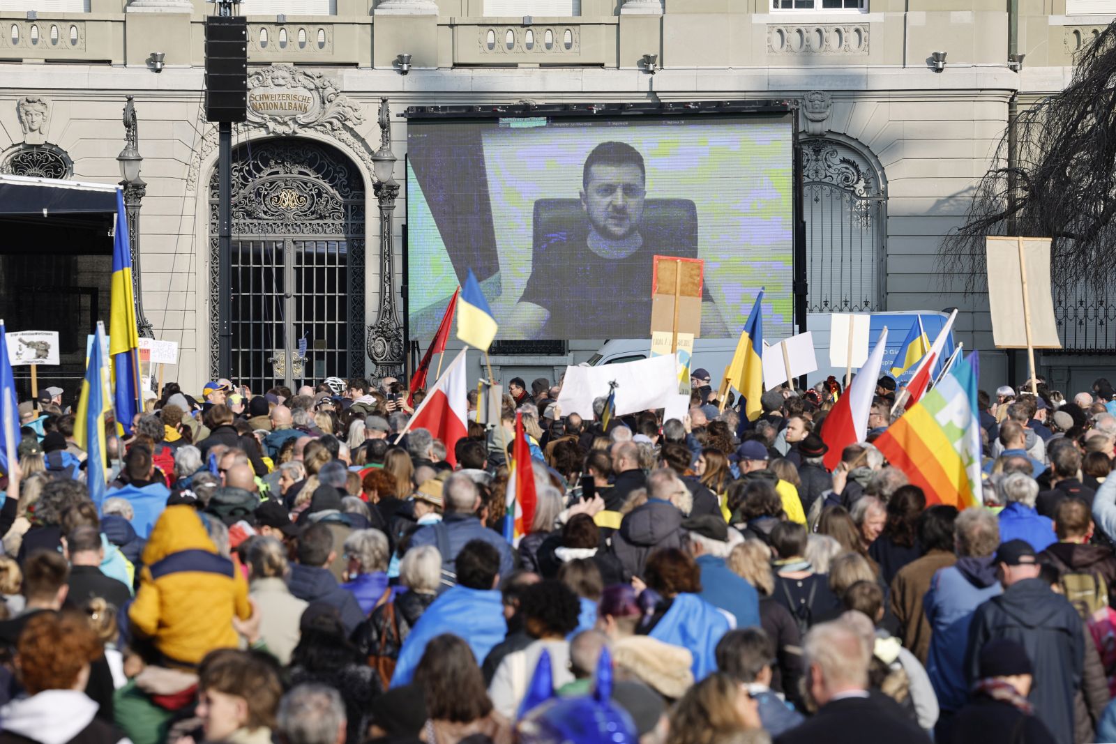 epa09835956 Ukrainian President Volodymyr Zelensky is displayed on a screen during a demonstration against the Russian invasion of Ukraine in front of the Swiss parliament building in Bern, Switzerland, 19 March 2022.  EPA/PETER KLAUNZER