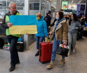 epa09842580 A volunteer holds a Ukrainian flag to guide refugees fleeing Ukraine following the Russian invasion from a platform as they arrive by train from Germany to Belgium at Midi Station in Brussels, Belgium, 22 March 2022. Brussels' Midi station very often is the the point of arrival for the Ukrainian refugees. After their arrival they are sent to the refugee center to be registered in order to have protection for at least one year.  EPA/STEPHANIE LECOCQ