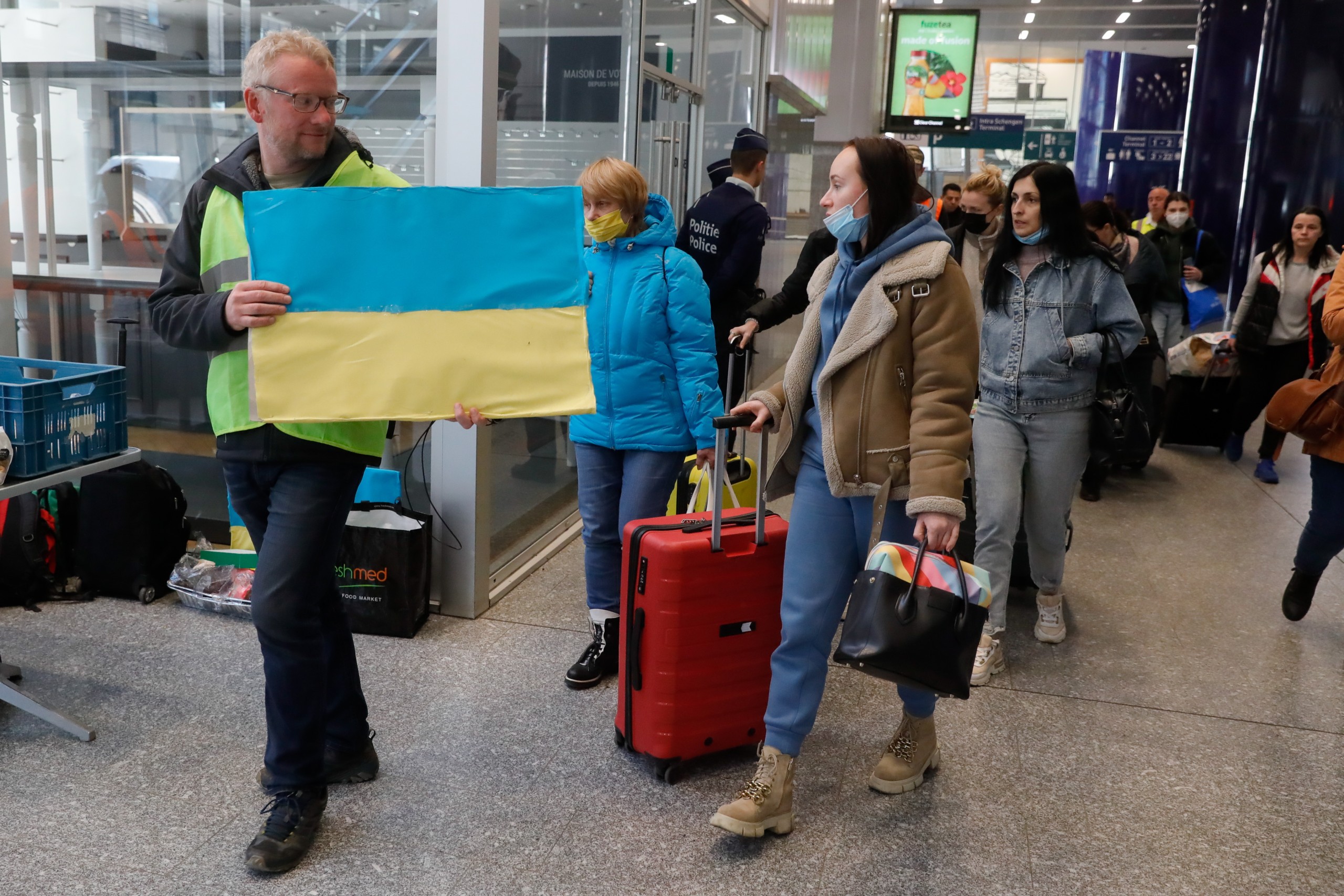 epa09842580 A volunteer holds a Ukrainian flag to guide refugees fleeing Ukraine following the Russian invasion from a platform as they arrive by train from Germany to Belgium at Midi Station in Brussels, Belgium, 22 March 2022. Brussels' Midi station very often is the the point of arrival for the Ukrainian refugees. After their arrival they are sent to the refugee center to be registered in order to have protection for at least one year.  EPA/STEPHANIE LECOCQ