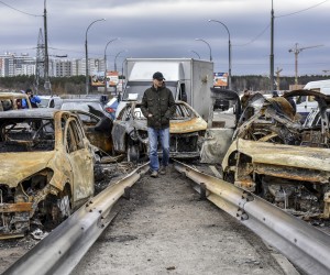 epa09873519 A man walks past burnt cars on a damaged bridge near the recaptured city of Irpin, Ukraine, 06 April 2022. Ukrainian forces have recently recaptured from the Russian army some cities and villages in the outskirts of Kyiv.  EPA/OLEG PETRASYUK